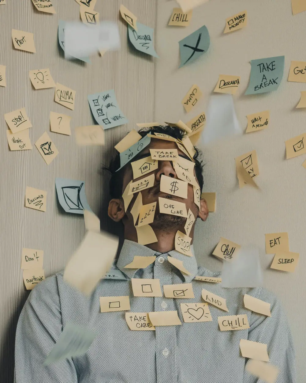 Post it notes falling all over a men and sticked top  a wall with tasks on them.